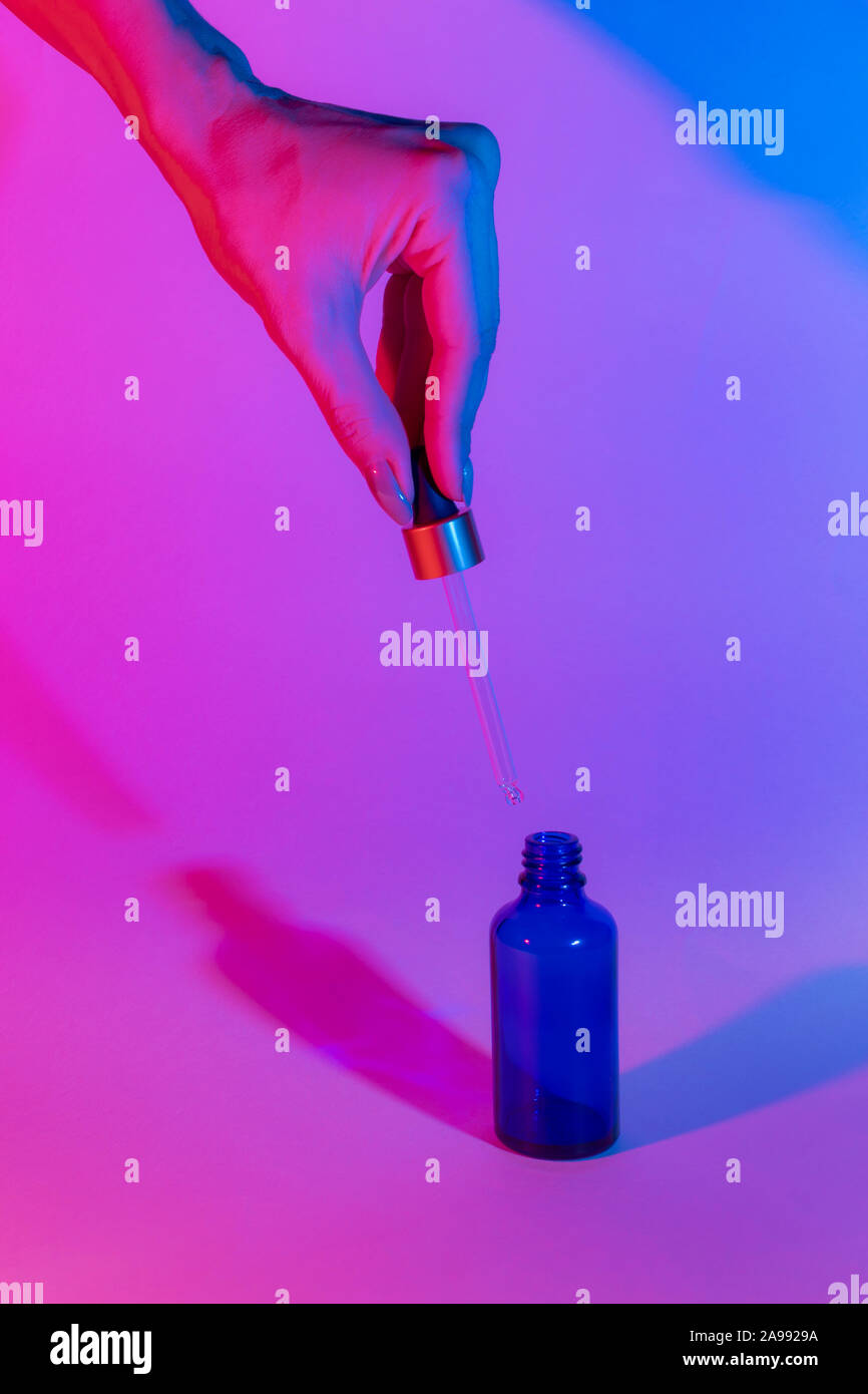 Download Bottle Of Blue On A Neon Trend Background Female Hand Holds A Glass Dropper Gradient From Pink To Blue Two Shadows Of Different Colors Stock Photo Alamy