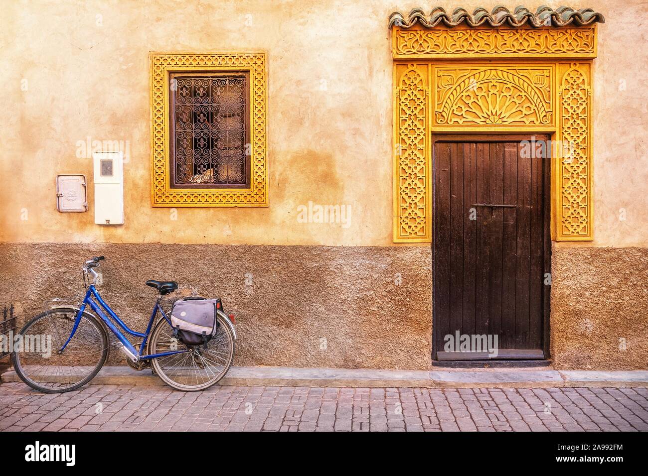 Street view of old house exterior in Morocco, with a wooden door, fancy gold colored window and door frames, and a bicycle parked in front. Stock Photo