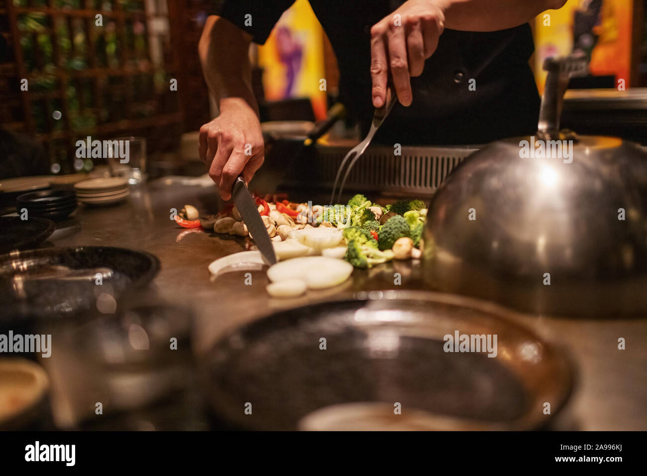 Teppanyaki chef preparing Japanese cuisine on hot metal plate by cutting up vegetables Stock Photo