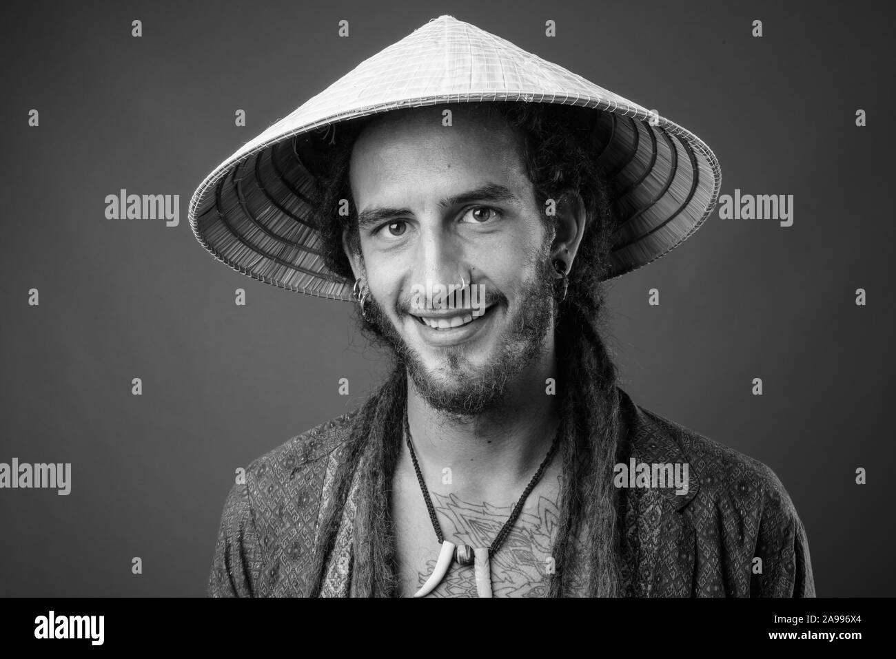 Young handsome Hispanic man with dreadlocks wearing Asian conical hat