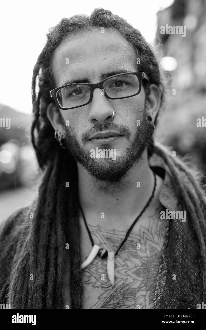 Young handsome Hispanic tourist man with dreadlocks outdoors in black and white Stock Photo