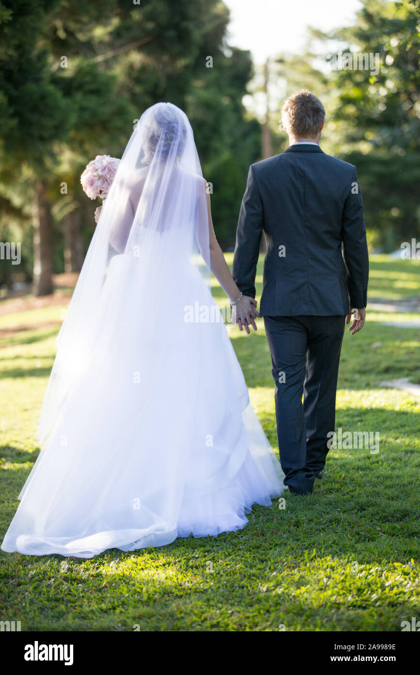 Bride and groom walk in the garden holding hands after their marriage ...