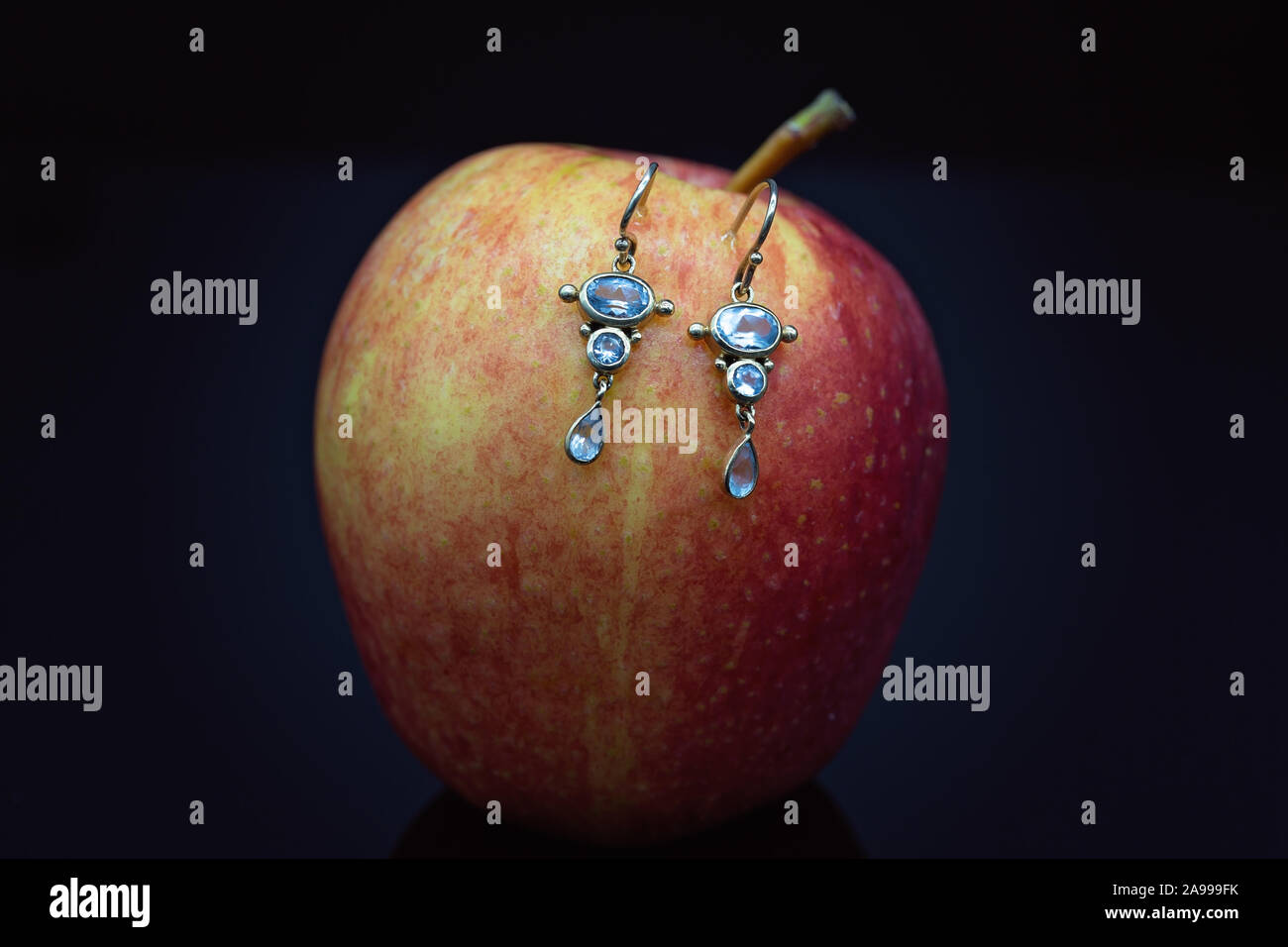 Delicate aquamarine ear-rings set in yellow gold displayed on an apple with a black background Stock Photo