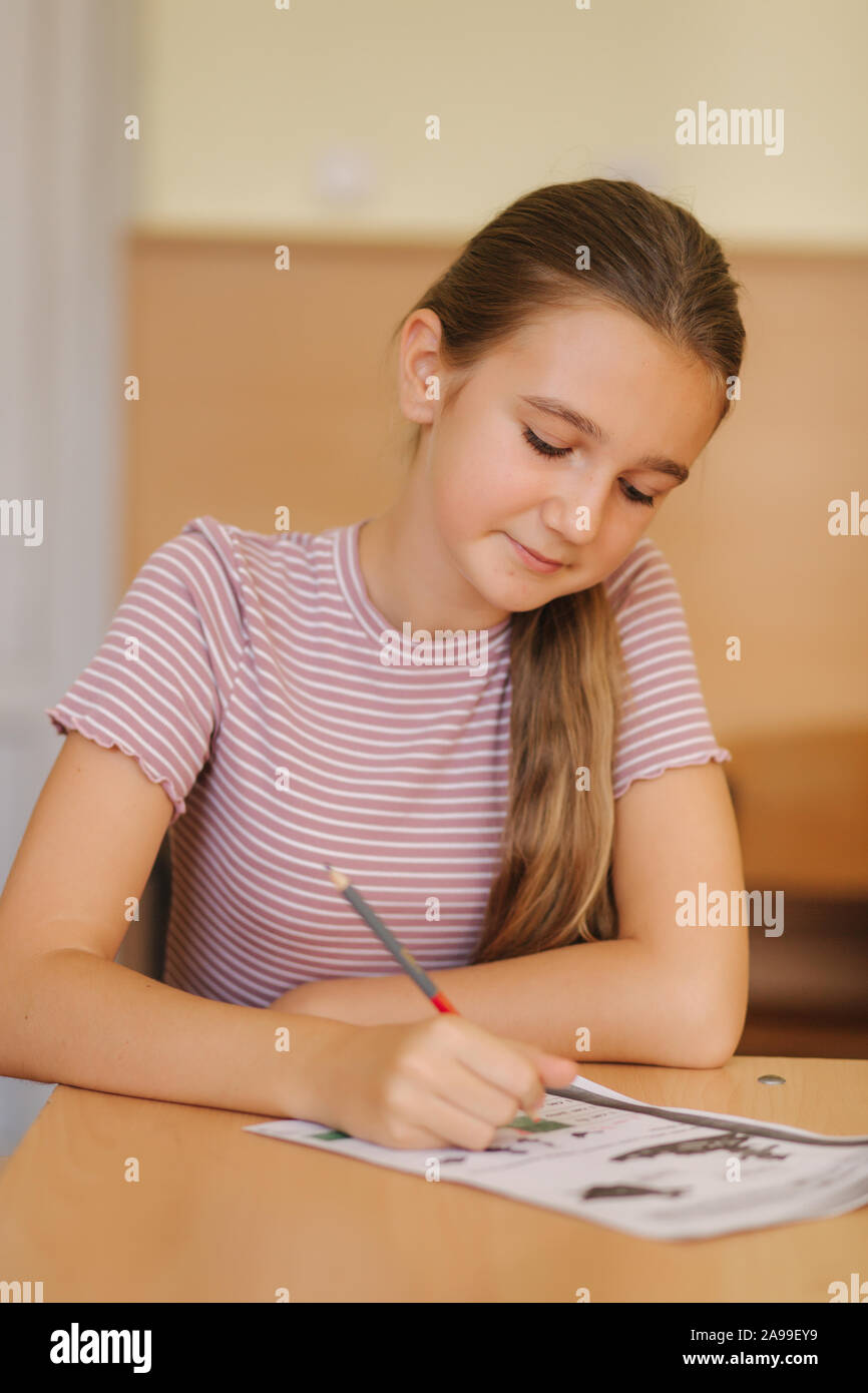 Happy Schoolgirl Sitting At Desk And Writing In Exercise Book