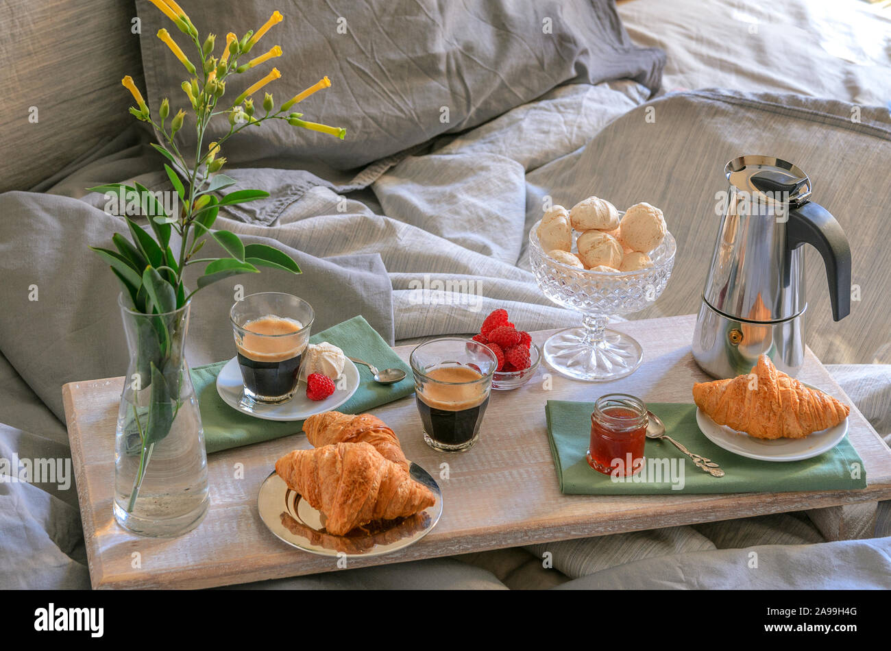 Luxury breakfast  in the bed in hotel bedroom . Coffee maker  and coffee glasses, croissants, jam, raspberry meringue and flowers on wood tray .Good m Stock Photo