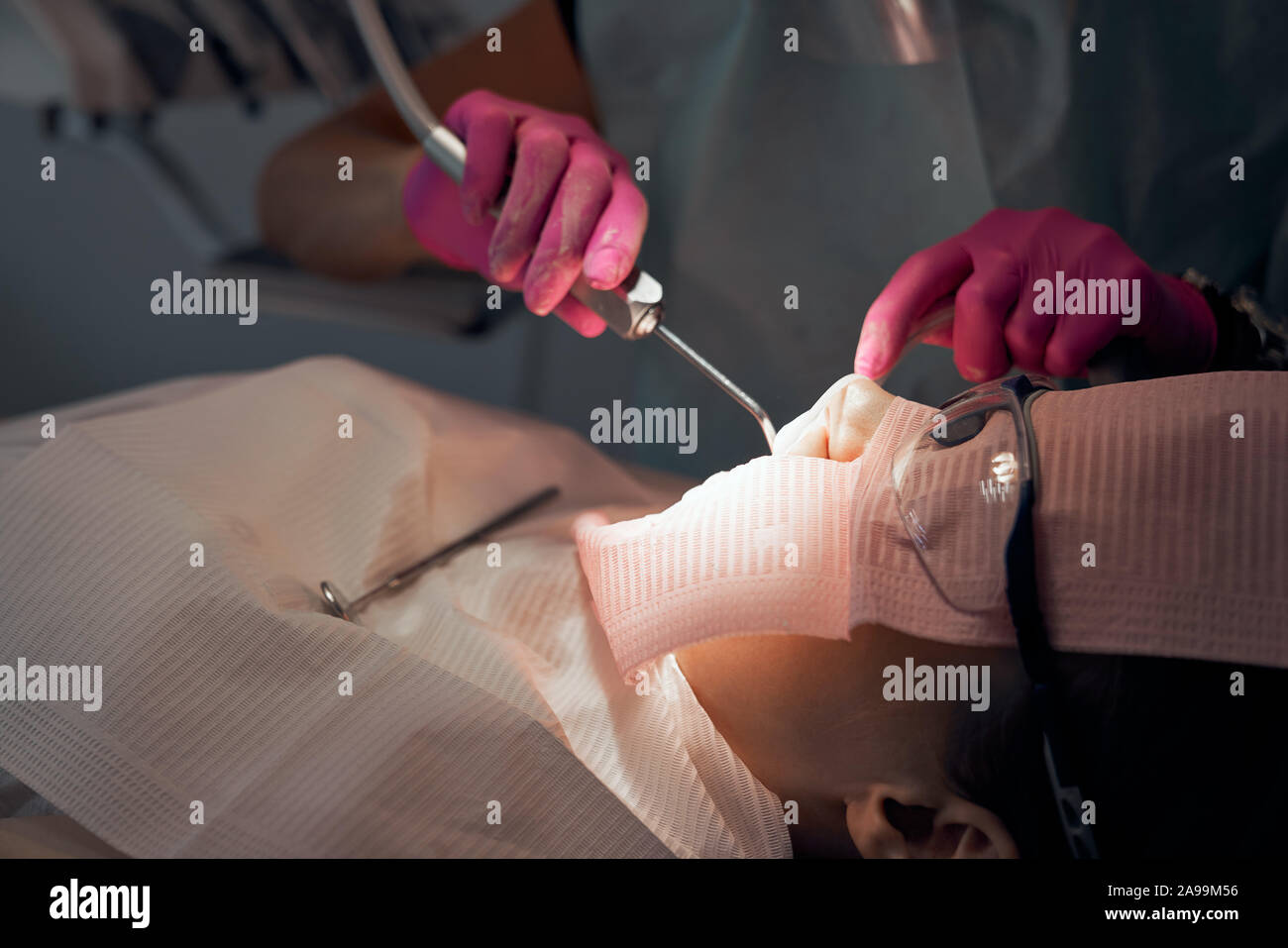 Dentist in rubber gloves doing procedure with dental curing UV light. Patient visiting dental clinic, sitting in dental chair with opening mouth. Doctor filling teeth. Stock Photo