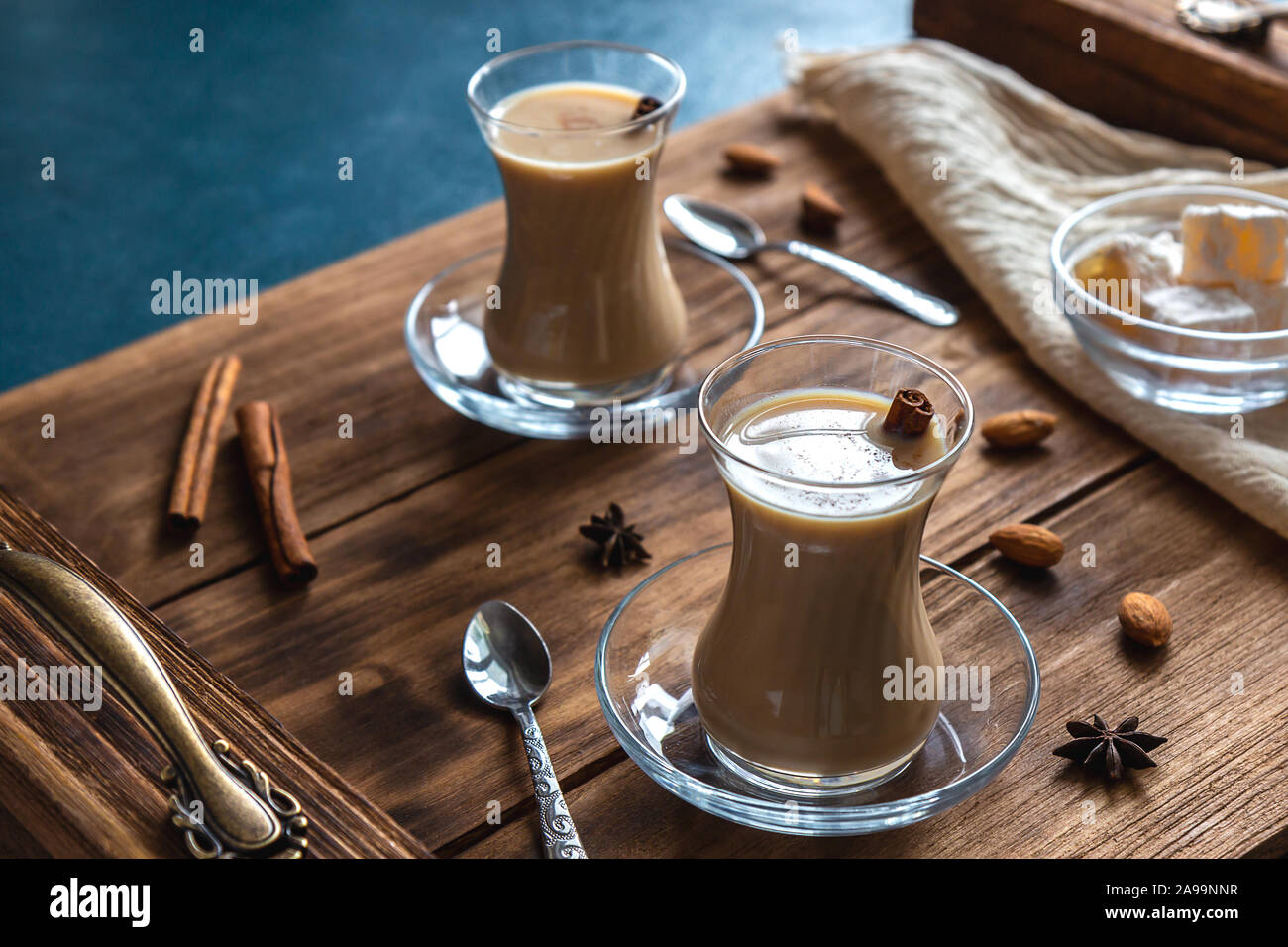 Indian tea with spices and milk. Masala chai in transparent glasses on a wooden tray. Horizontal orientation. Stock Photo