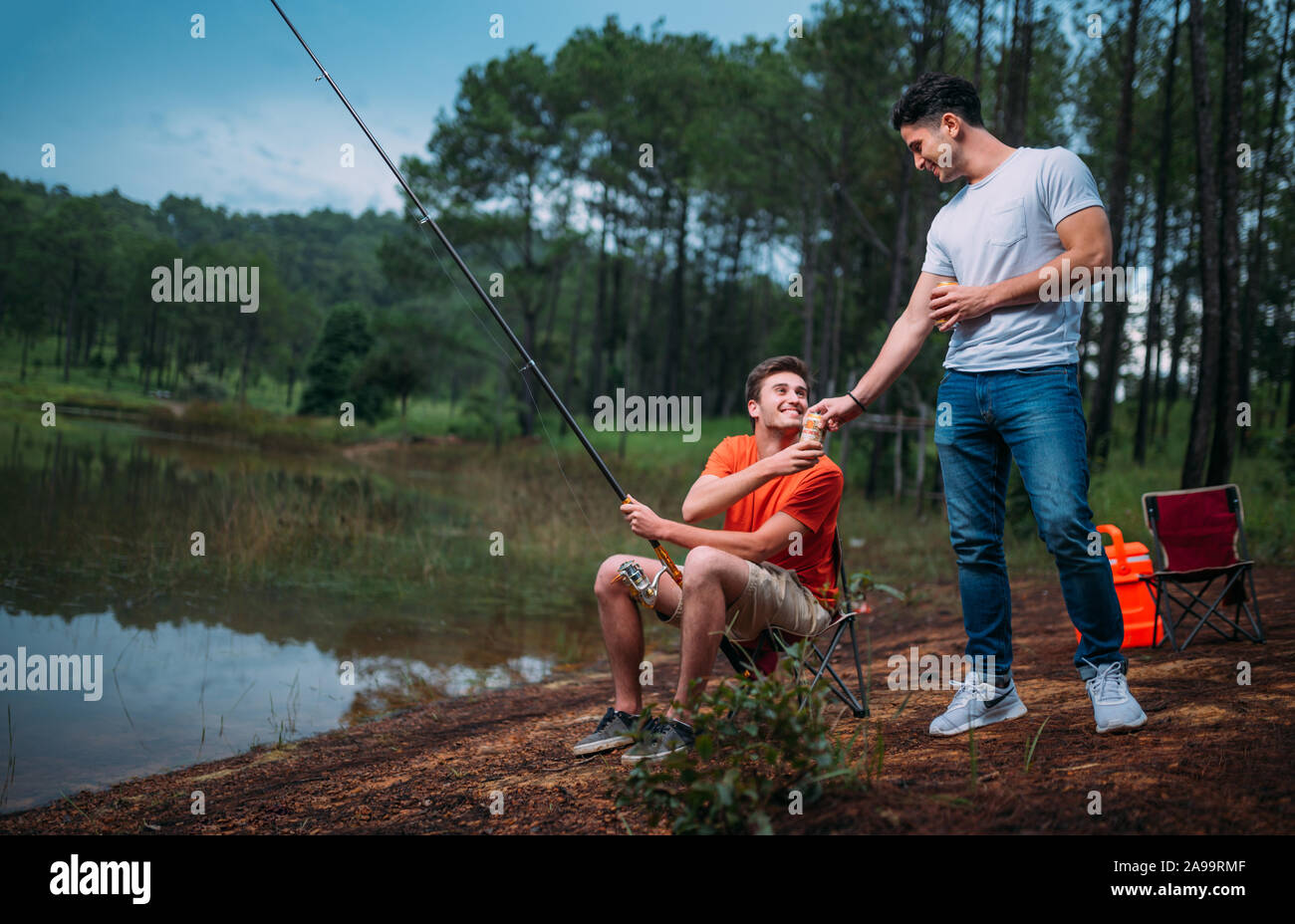 Two friends sitting together with beer on the picnic while fishing near the lake Stock Photo