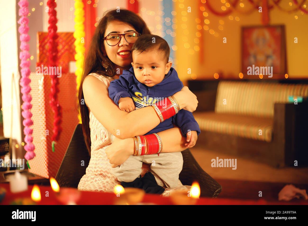 Portrait of a beautiful young Indian woman in traditional dress holding an acute baby boy within the decorative background on the occasion of Diwali. Stock Photo