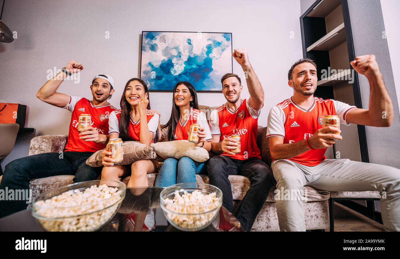 Party friends or arsenal fans watching soccer on tv and drinking Ganzberg beer celebrating victory at home Stock Photo