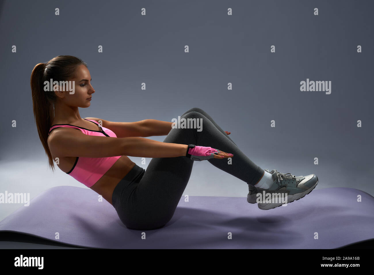 Brunette slim sporty girl with tanned skin in sportswear doing v-ups abs  workout on yoga mat. Young strong female looks very concentrated while  keeping balance during her daily training Stock Photo -