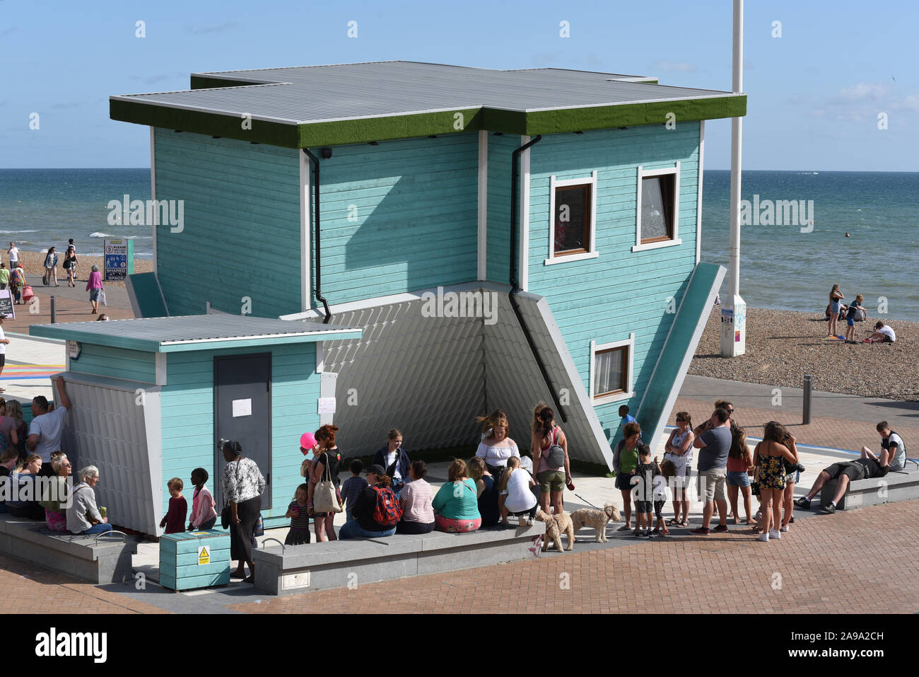 Visitors wait outside The Upside Down House on Brighton & Hove seafront Stock Photo