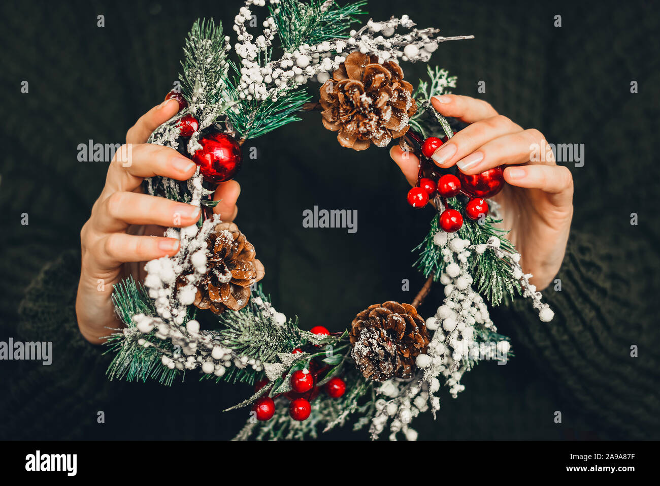 Pine wreath and Christmas decor in female hands on a green knitted background. Christmas, New Year, preparation for the holiday. Stock Photo