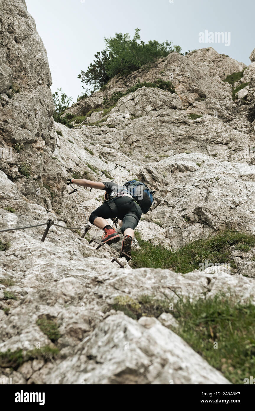 Male mountain climber in steep vertical wall climbing the via ferrata in Julian Alps. Alpinism, mountain climbing and protective gear concepts Stock Photo