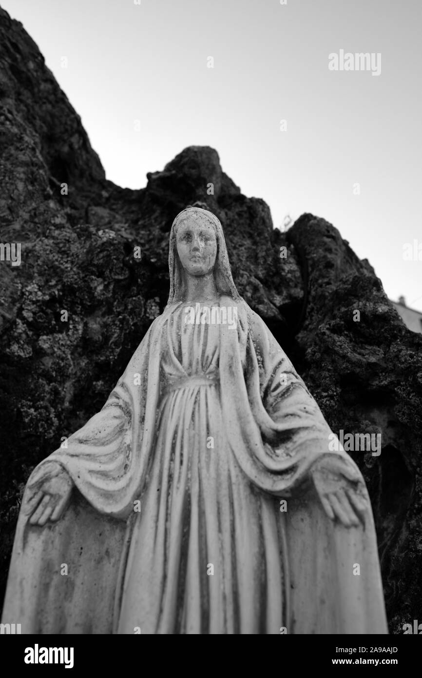 A Virgin Mary statue figure with open arms in Corte Haute-Corse Corsica France - guardian angel looking down B/W Stock Photo