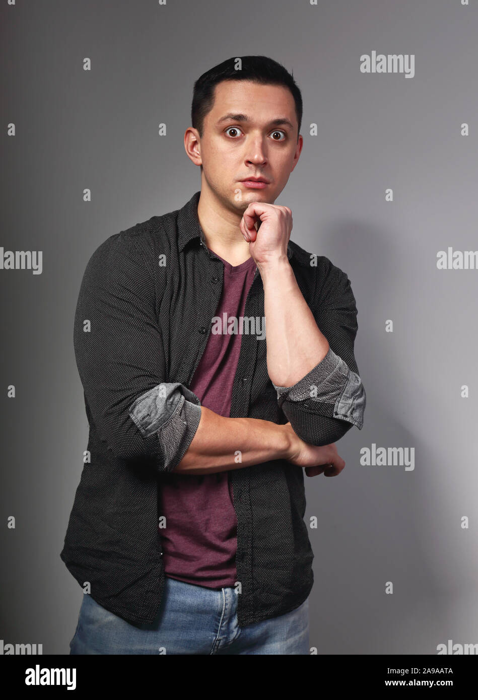 Surprising brunette man thinking and looking with big eyes in purlple t shirt with folded arms on dark grey background. Closeup portrait Stock Photo Alamy