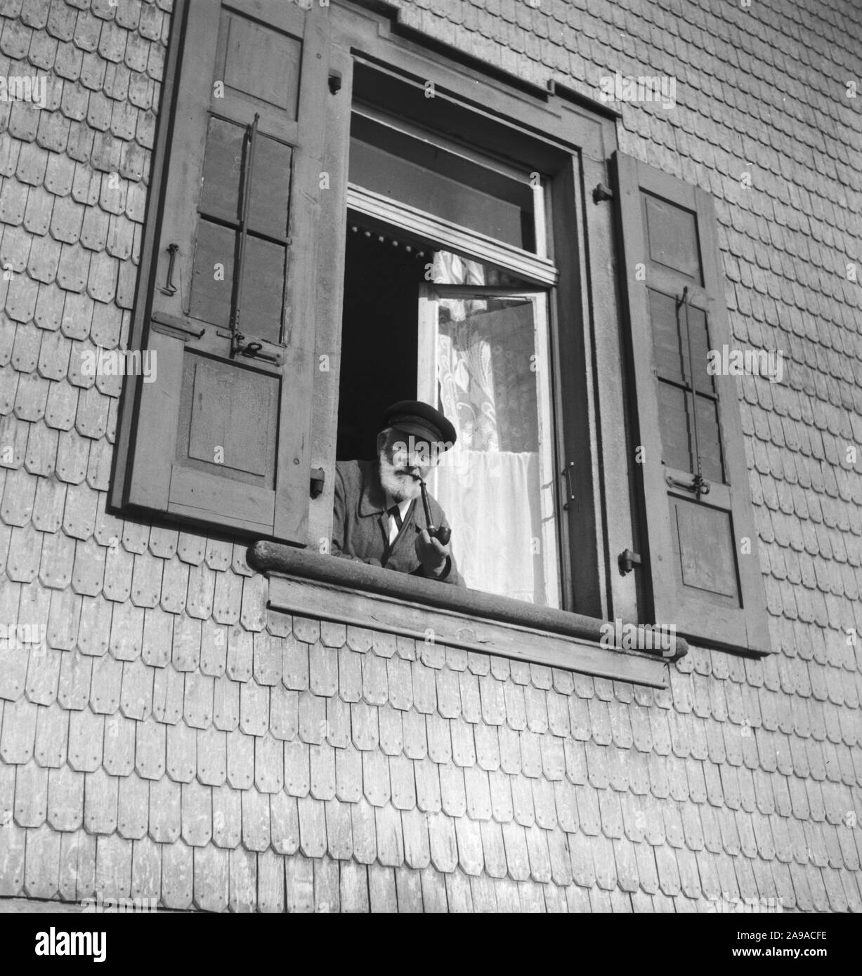 An old man looking out of the window, smoking a pipe, Germany 1930s. Stock Photo