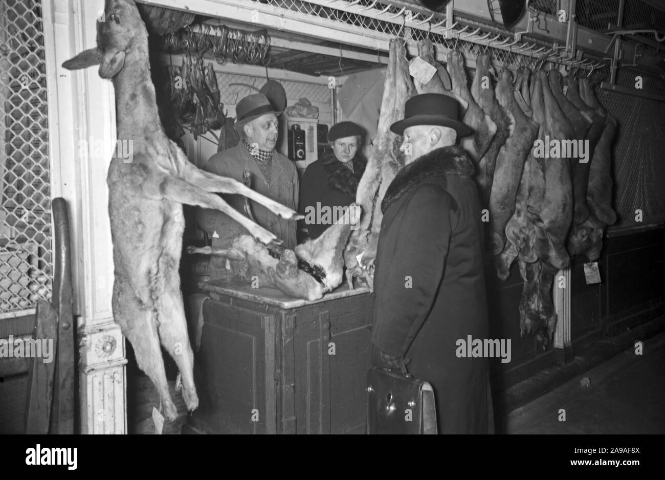 People shopping for food on the market, here: booth of deer meat, Germany 1930s. Stock Photo