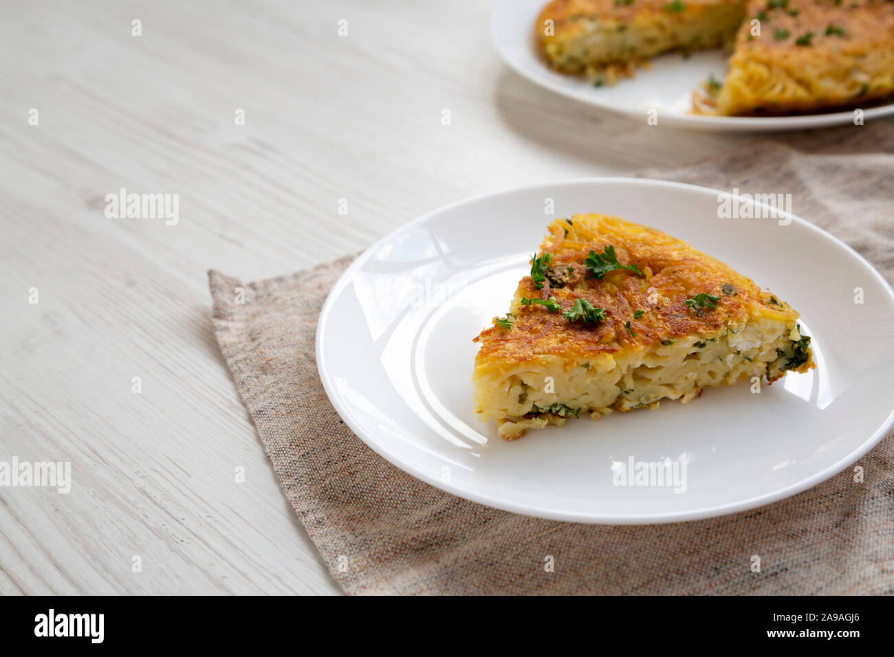 A piece of spaghetti omelette on a white plate on a white wooden background, side view. Copy space. Stock Photo