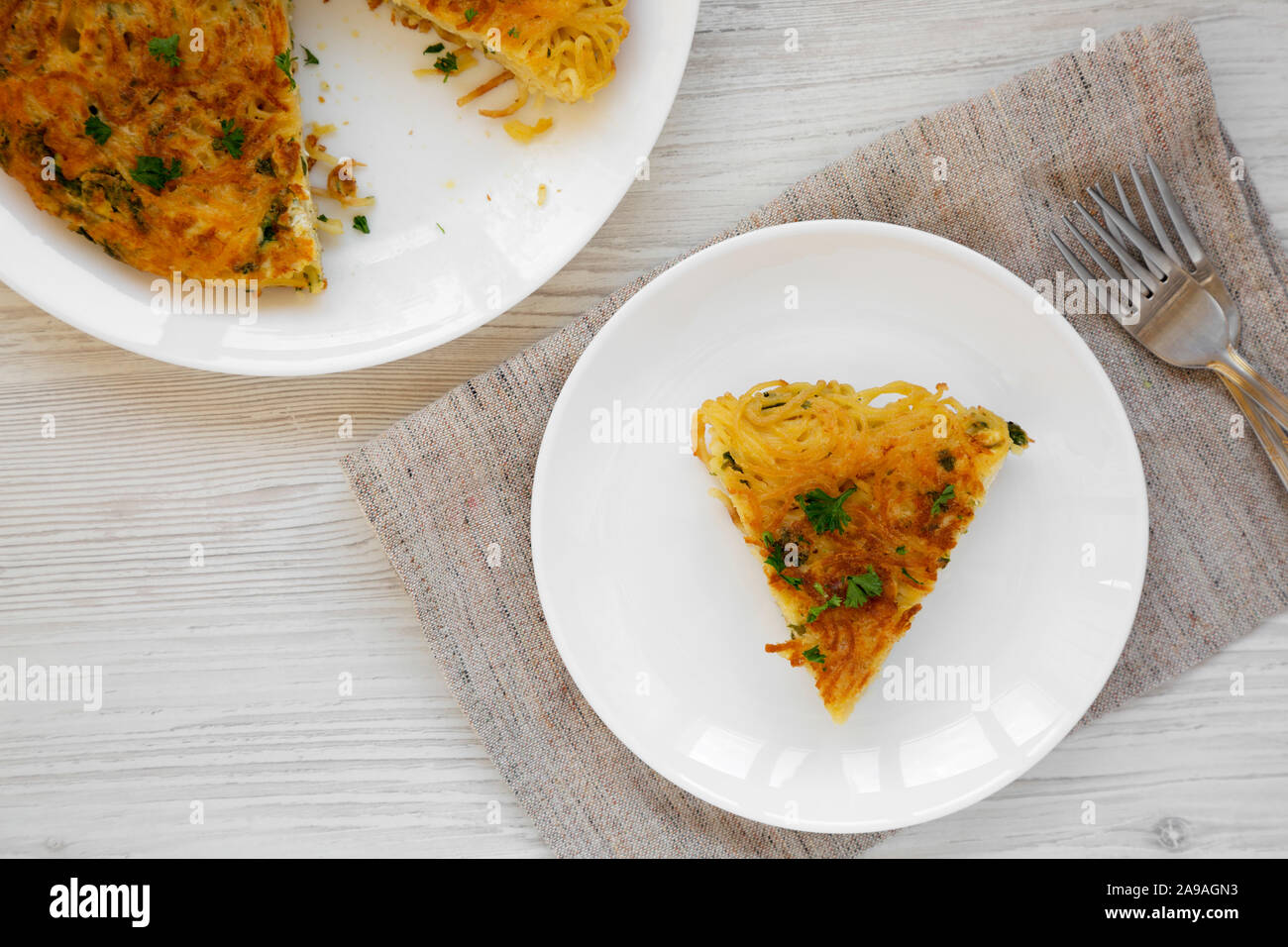 Homemade spaghetti omelette on a white plate on a white wooden background, top view. Flat lay, overhead, from above. Stock Photo