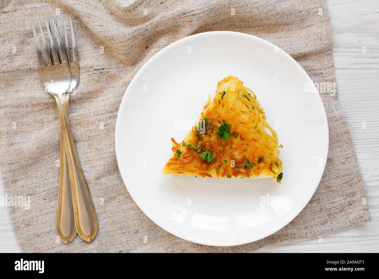 Homemade spaghetti omelette on a white plate on a white wooden background, overhead view. Flat lay, top view, from above. Stock Photo