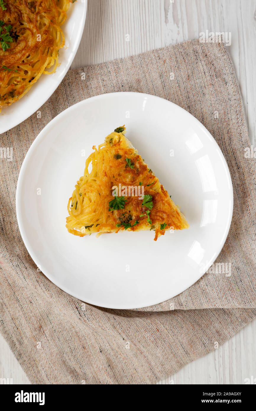 Homemade spaghetti omelette on a white plate on a white wooden table, overhead view. Flat lay, top view, from above. Stock Photo