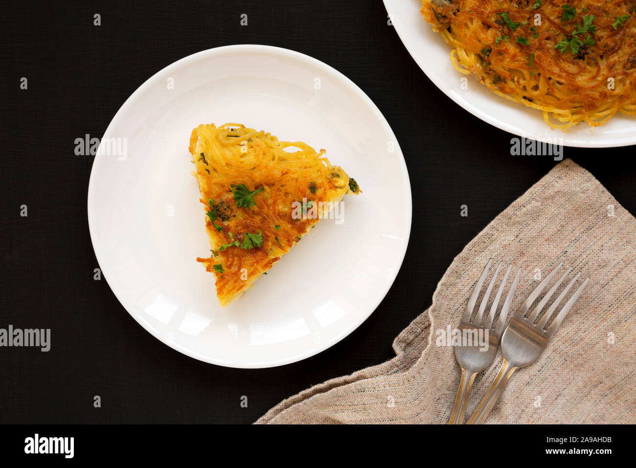 Homemade spaghetti omelette on a white plate over black surface, top view. Flat lay, overhead, from above. Close-up. Stock Photo