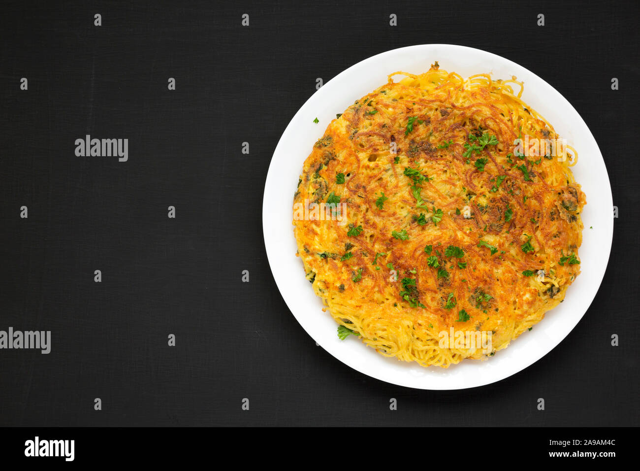 Homemade spaghetti omelette on a white plate on a black surface, top view. Flat lay, overhead, from above. Copy space. Stock Photo