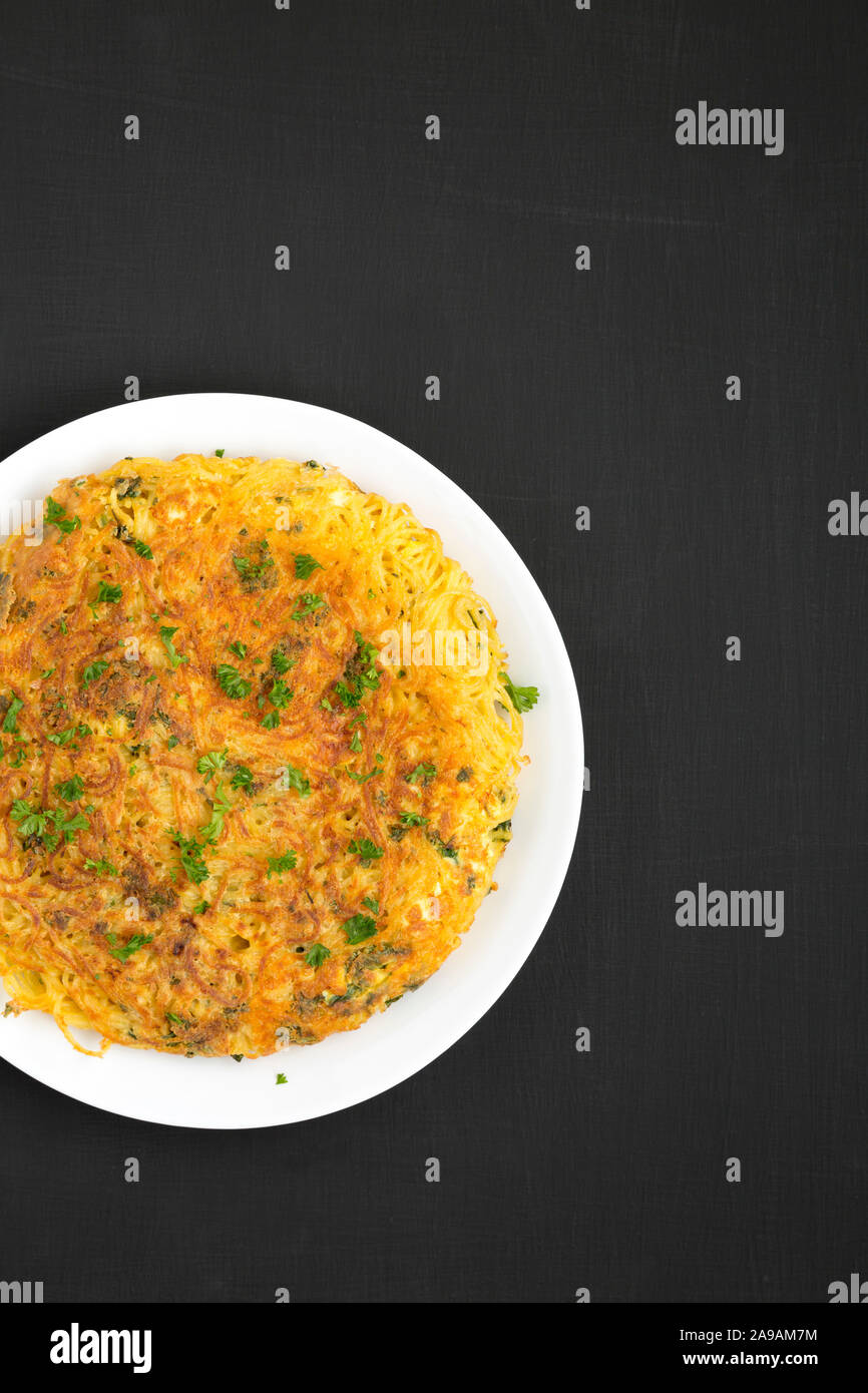 Homemade spaghetti omelette on a white plate on a black background, top view. Flat lay, overhead, from above. Space for text. Stock Photo