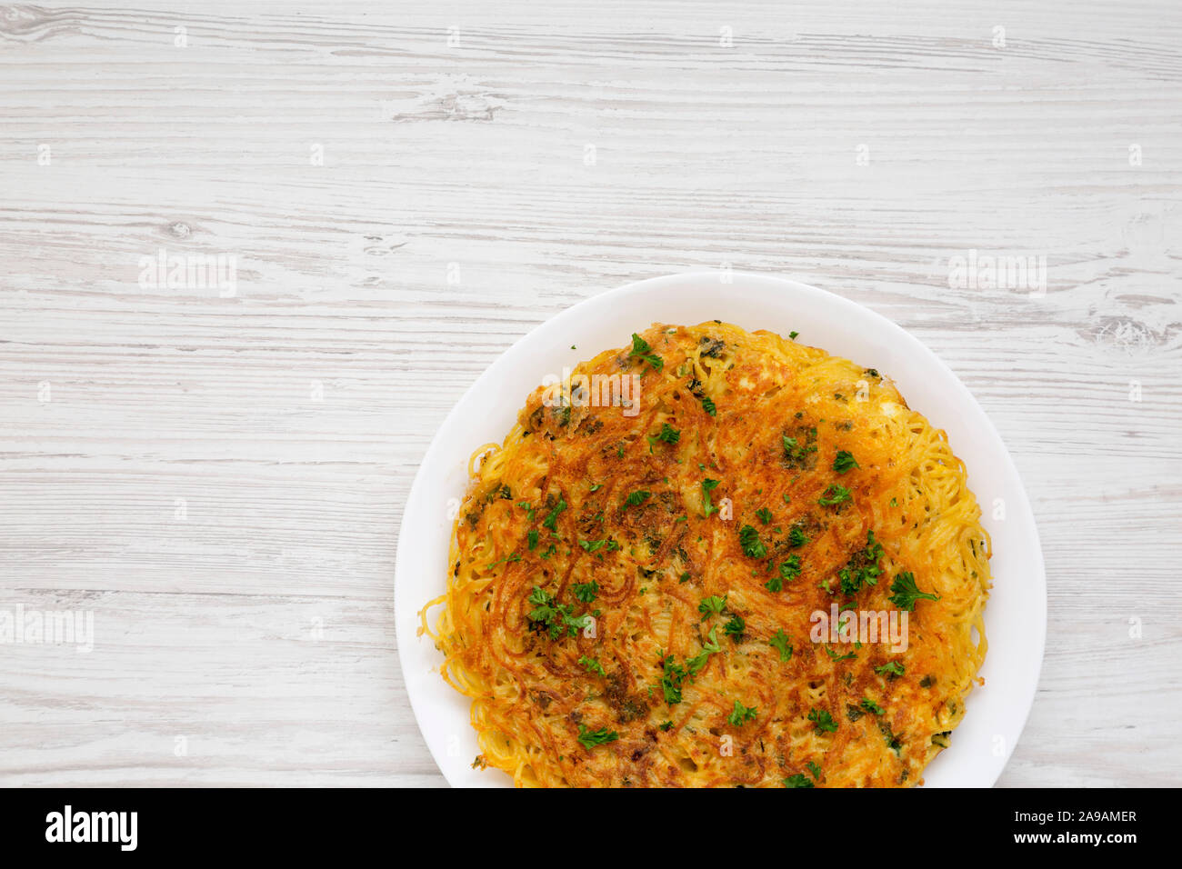 Homemade spaghetti omelette on a white plate over white wooden surface, view from above. Flat lay, overhead, from above. Copy space. Stock Photo
