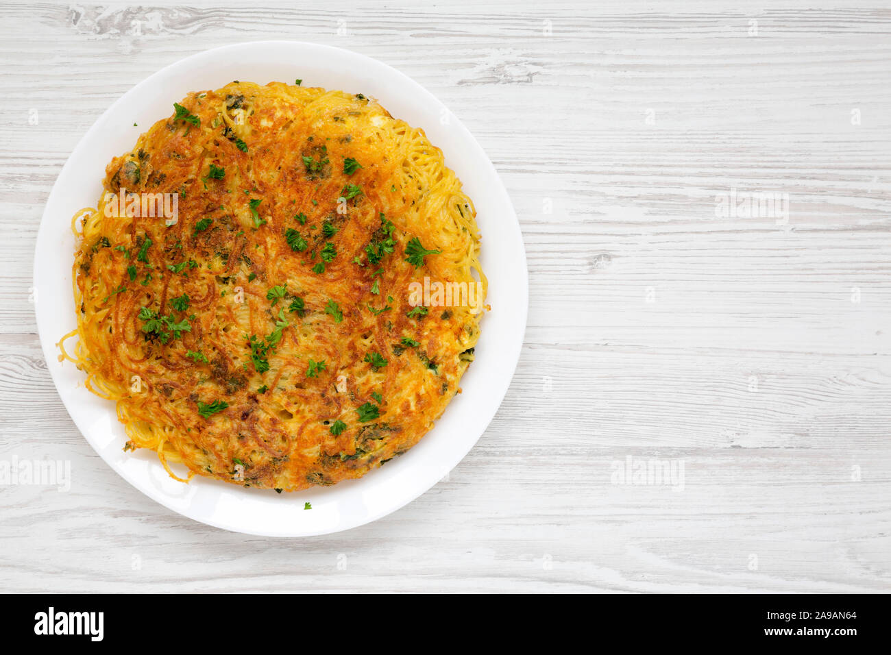 Homemade spaghetti omelette on a white plate over white wooden surface, overhead view. Flat lay, top view, from above. Stock Photo