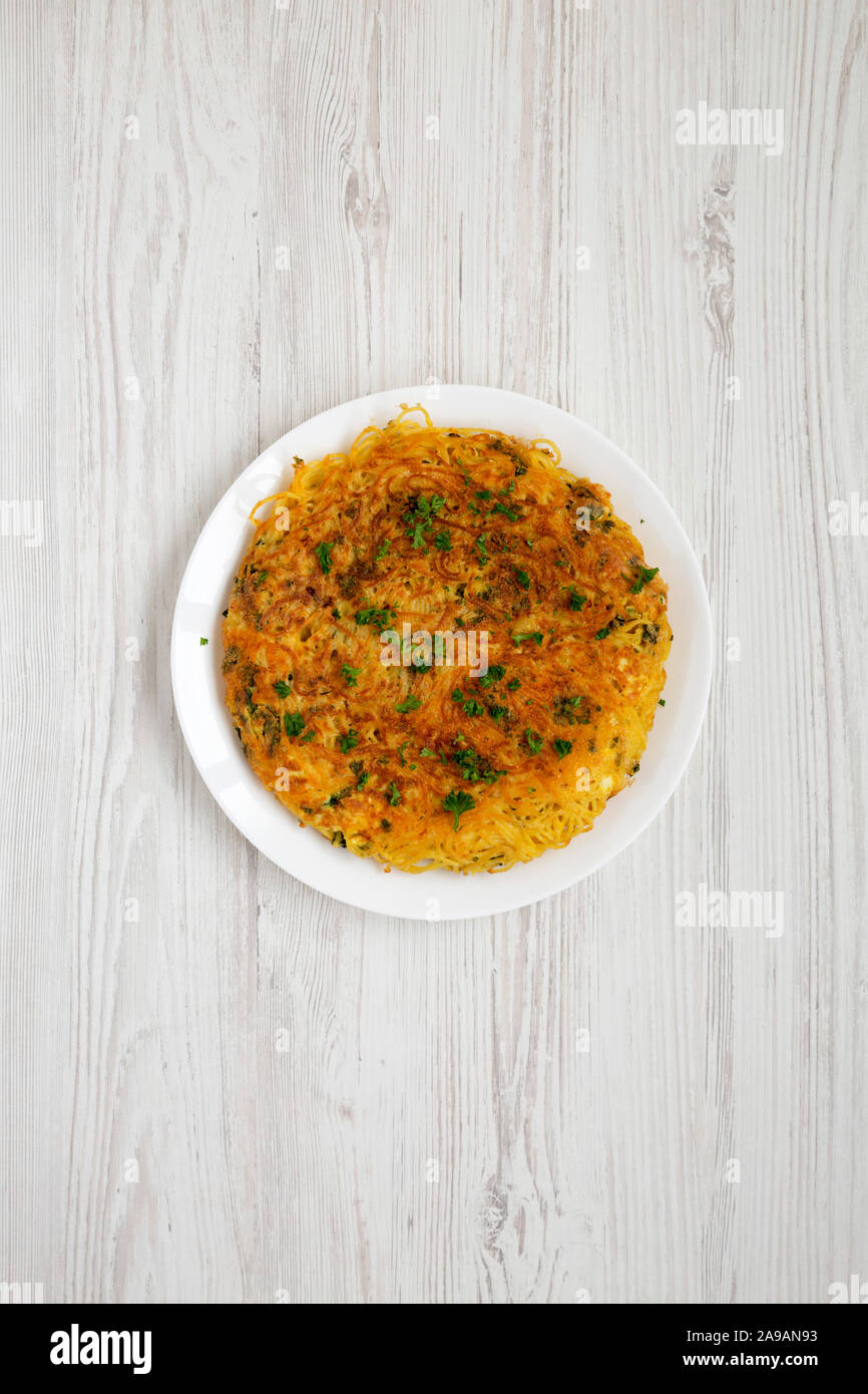 Homemade spaghetti omelette on a white plate over white wooden background, top view. Flat lay, overhead, from above. Stock Photo