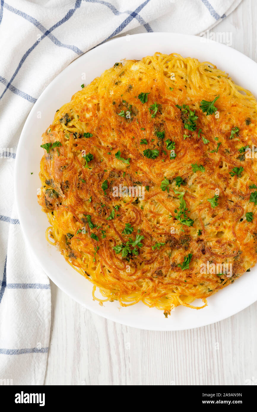 Homemade spaghetti omelette on a white plate over white wooden surface, top view. Flat lay, overhead, from above. Close-up. Stock Photo