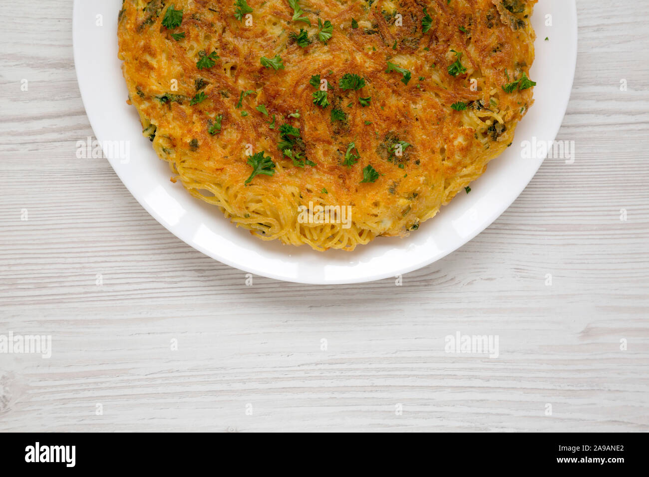 Homemade spaghetti omelette on a white plate over white wooden surface, top view. Space for text. Stock Photo