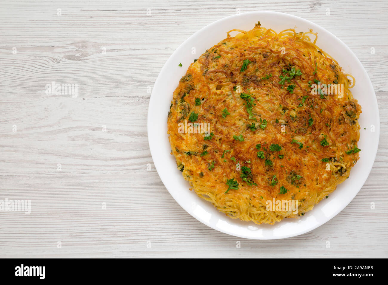 Homemade spaghetti omelette on a white plate over white wooden background, top view. Copy space. Stock Photo