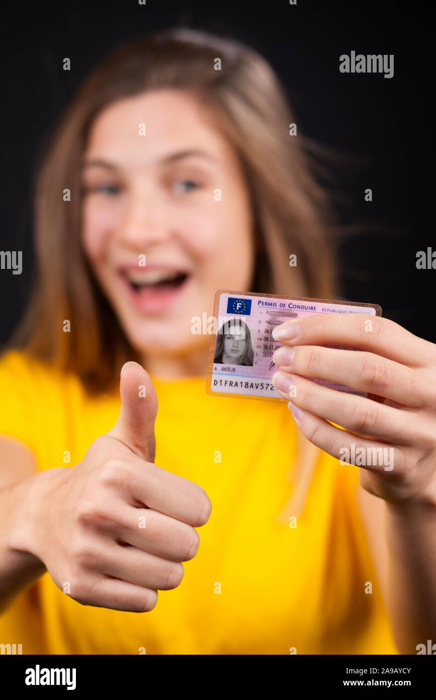 Beautiful and natural teenager showing proudly her French drivers license (permis de conduire). Black background, portrait. Stock Photo