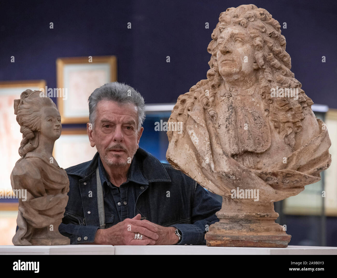 Bonhams, London, UK. 14th November 2019. Nicky Haslam, one of the world’s most celebrated interior designers, attends a photo call at Bonhams for the sale of his impressive collection from the Hunting Lodge in Hampshire, where Haslam has lived since 1978. Image: Nicky Haslam  with (right) French Terracotta washed plaster Bust of an 18th Century Nobleman.  Estimate: £800-1200. Credit: Malcolm Park/Alamy Live News. Stock Photo