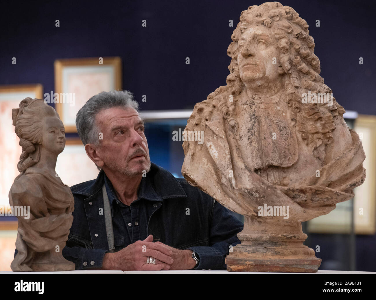 Bonhams, London, UK. 14th November 2019. Nicky Haslam, one of the world’s most celebrated interior designers, attends a photo call at Bonhams for the sale of his impressive collection from the Hunting Lodge in Hampshire, where Haslam has lived since 1978. Image: Nicky Haslam  with (right) French Terracotta washed plaster Bust of an 18th Century Nobleman.  Estimate: £800-1200. Credit: Malcolm Park/Alamy Live News. Stock Photo