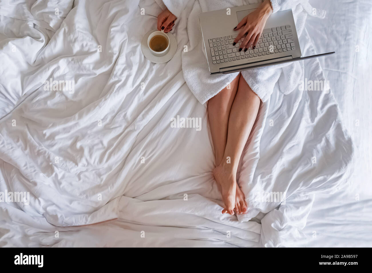 Woman In White Bathrobe Sitting On The Bed With Cup Of Coffee And Working On Her Laptop Stock 4670