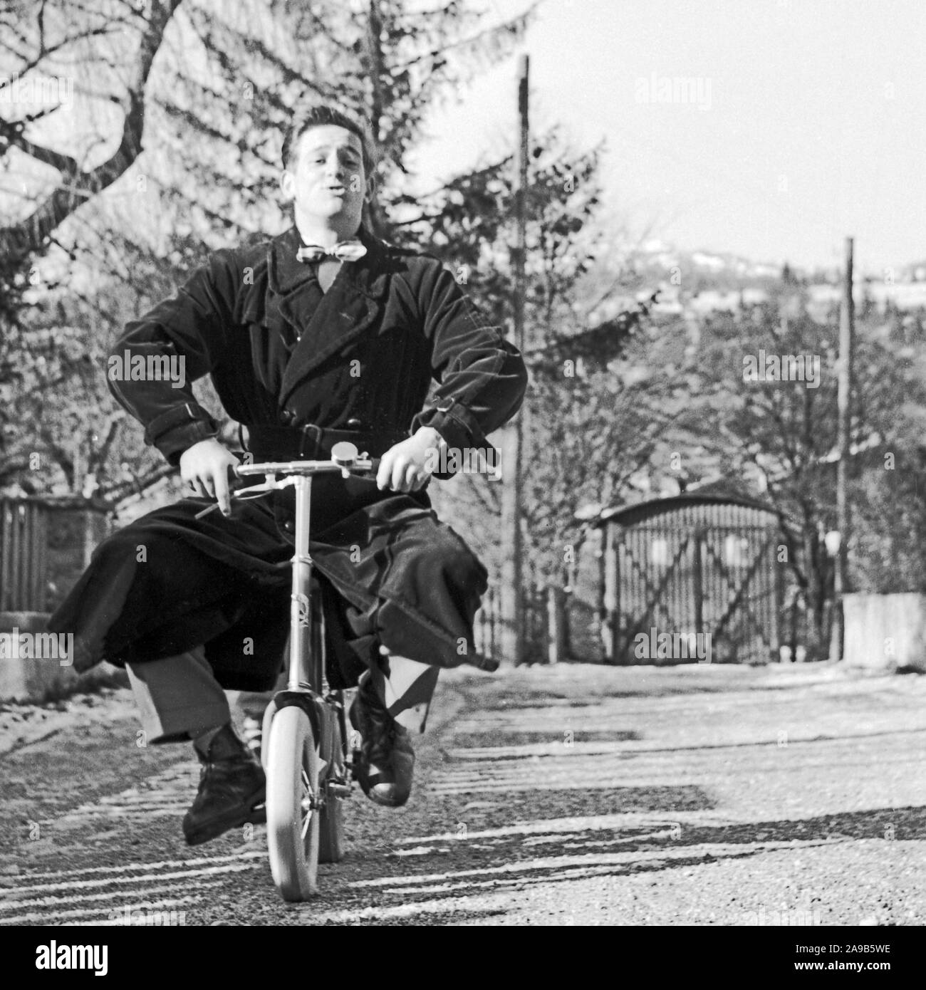A young man trying to ride a children's bicycle, Germany 1956 Stock Photo