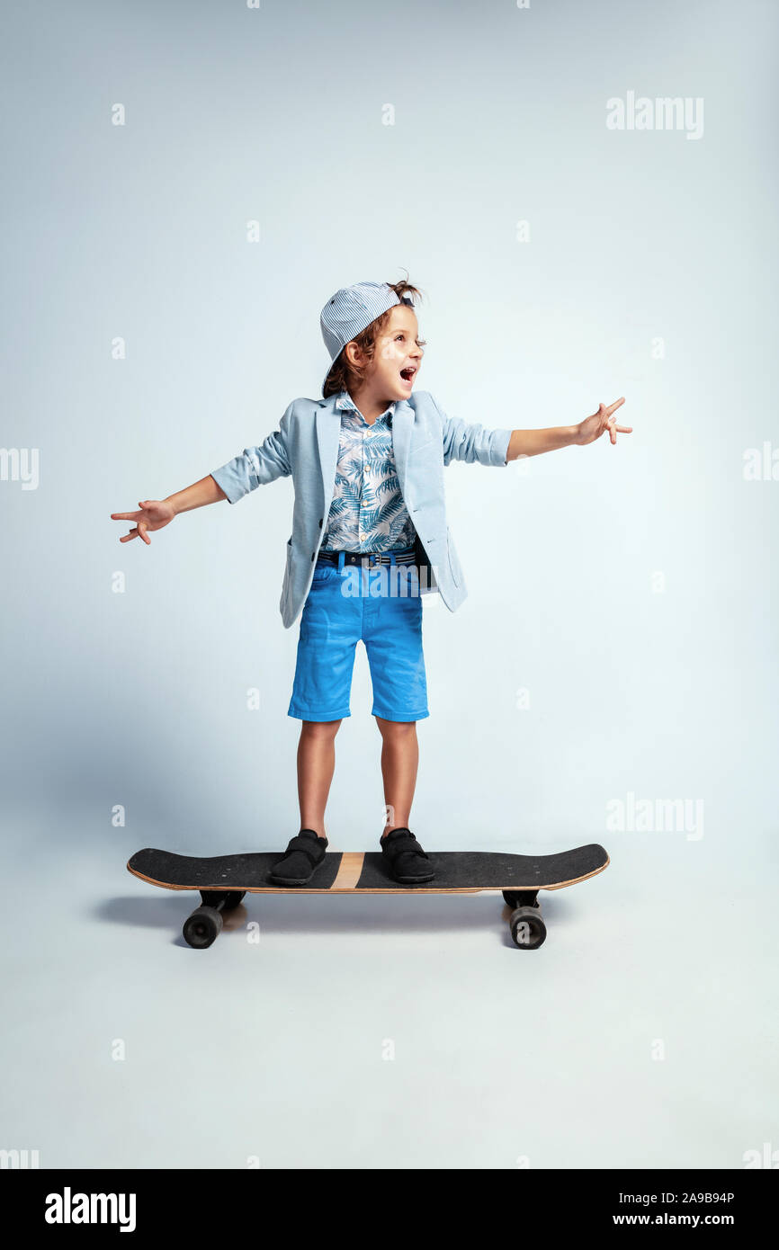 Pretty young boy on skateboard in casual clothes on white studio