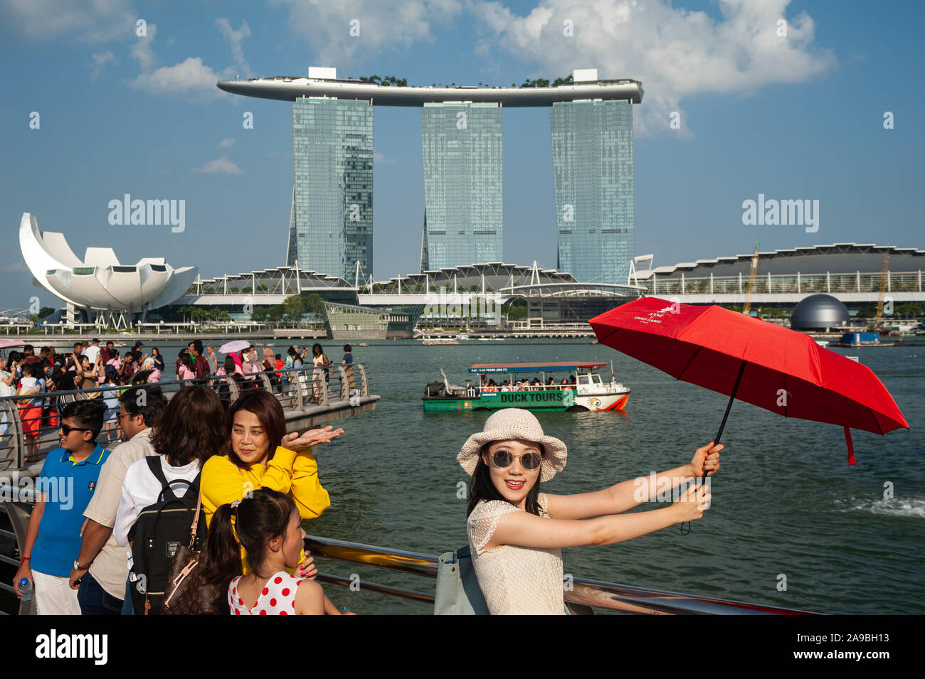 01.08.2019, Singapore, , Singapore - Tourists posing in Merlion Park on the banks of the Singapore River for photos with the Marina Bay Sands Hotel in Stock Photo