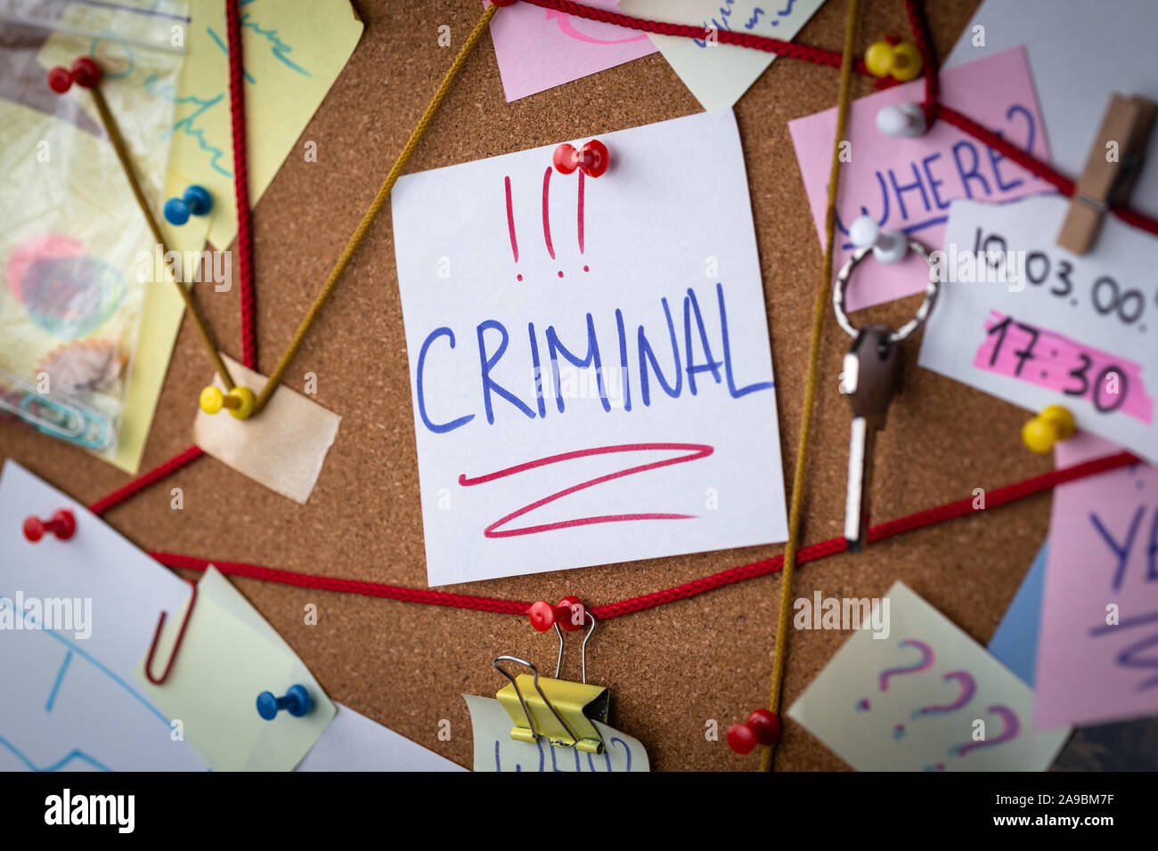 Crime search concept. Close-up view of a detective board with evidence. In the center is a white sheet attached with a red pin with the text Criminal. Stock Photo