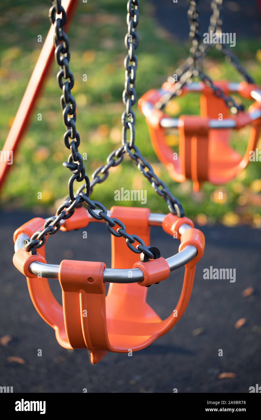 Photograph of an empty bright orange children's swing on empty playground, no people Stock Photo