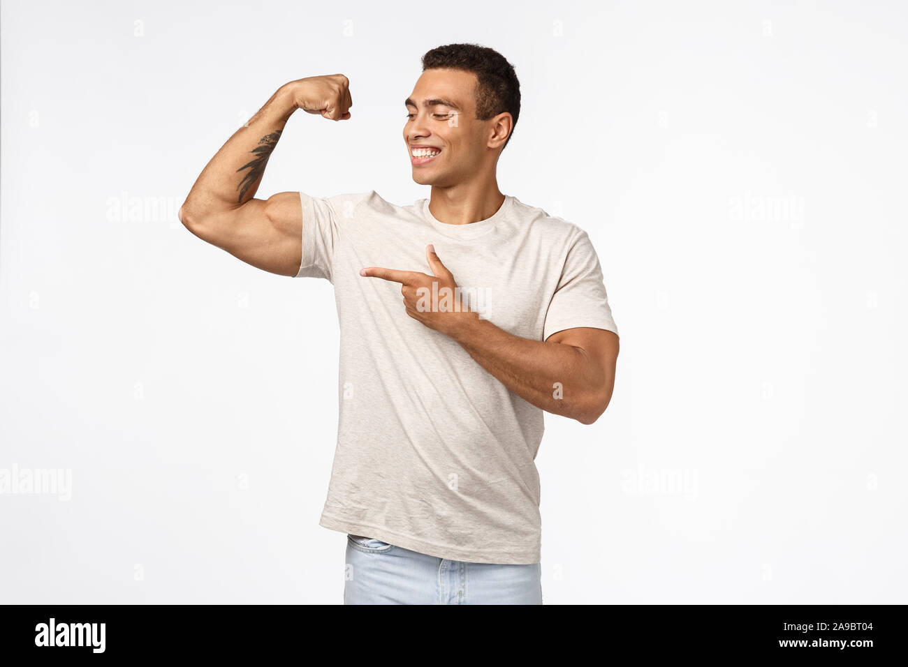 Satisfied, proud assertive young brazilian man with strong muscles, tense raised arm, smiling and pointing biceps proudly, delighted with own perfect Stock Photo