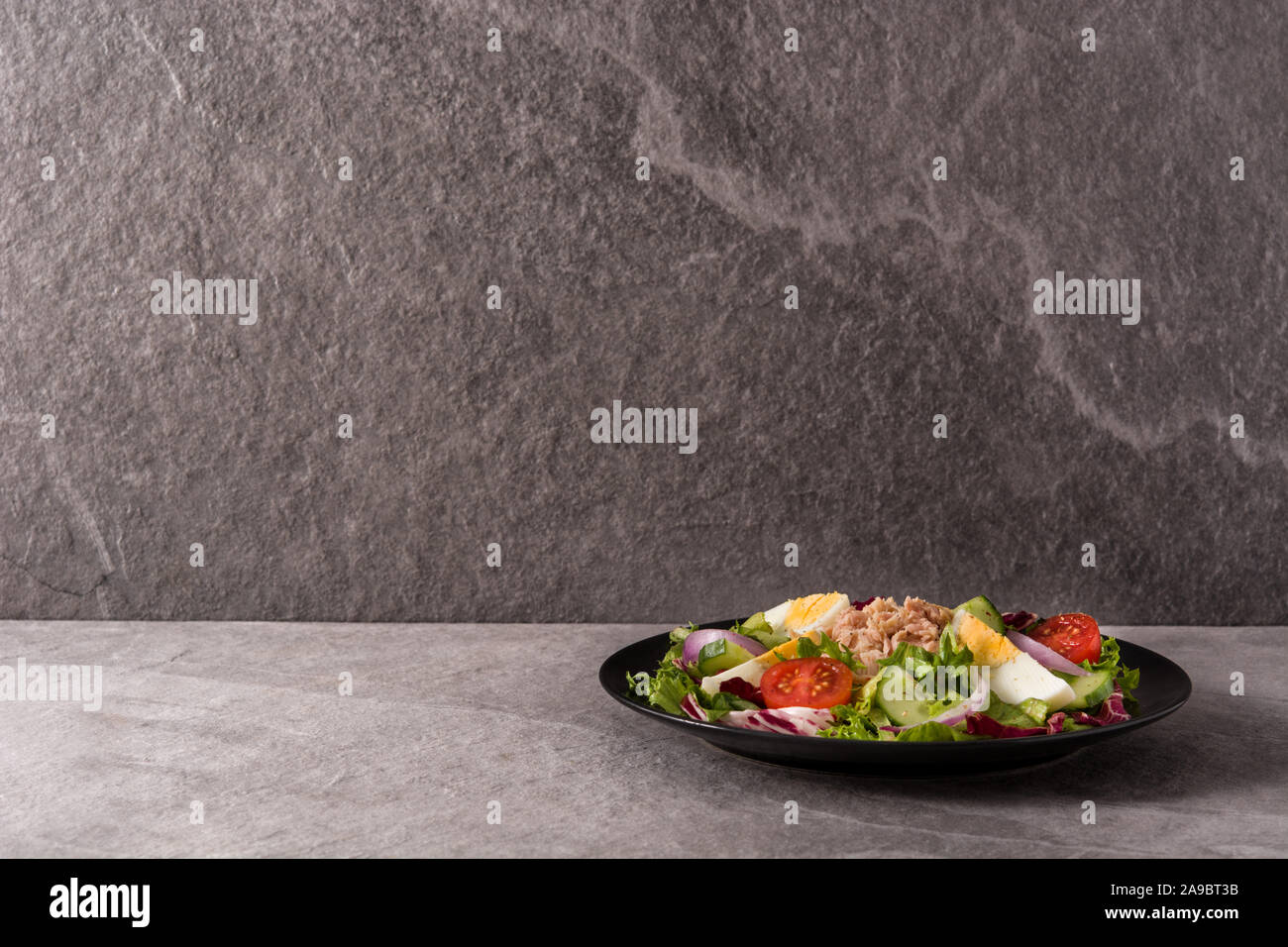 Salad with tuna, egg and vegetables on black plate and gray background. Stock Photo