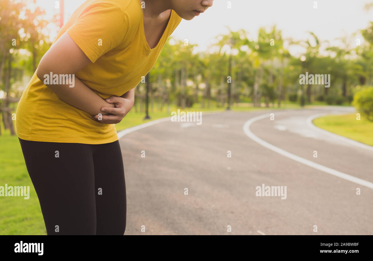 Sport womanman holding abdomen with her hands in stomach pain after running workout at park