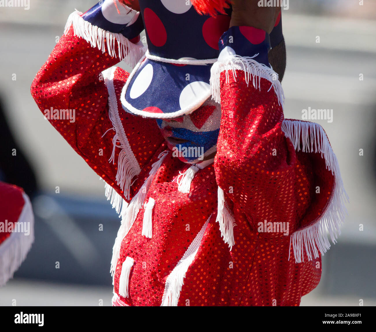 small child, young boy, kid, youngster wearing sparkly red sequinned jacket and epaulettes adjusting a polka dot hat in a carnival parade on New Year Stock Photo