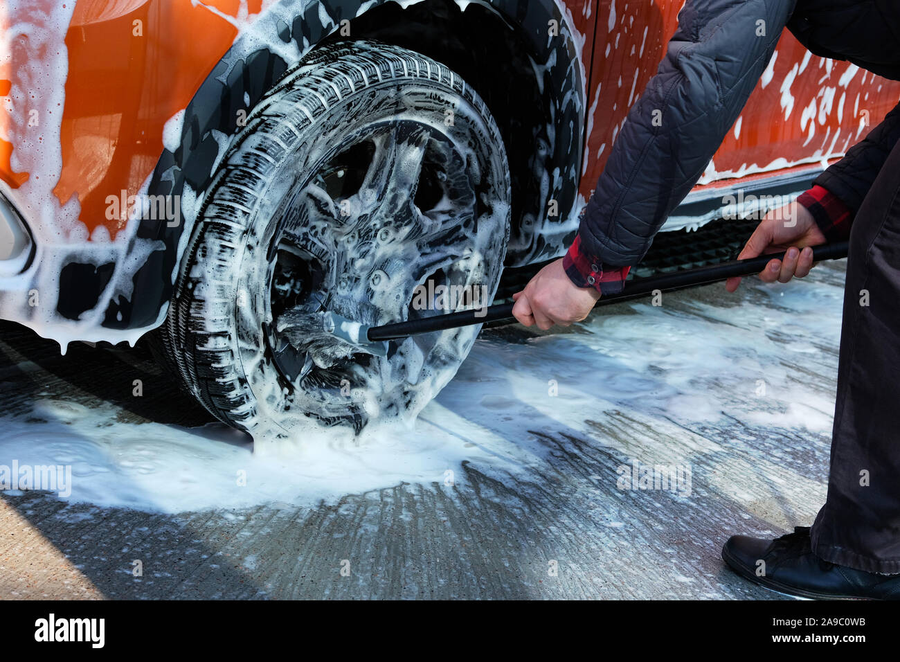 Cleaning with soap suds at selfservice car wash. Man washes black