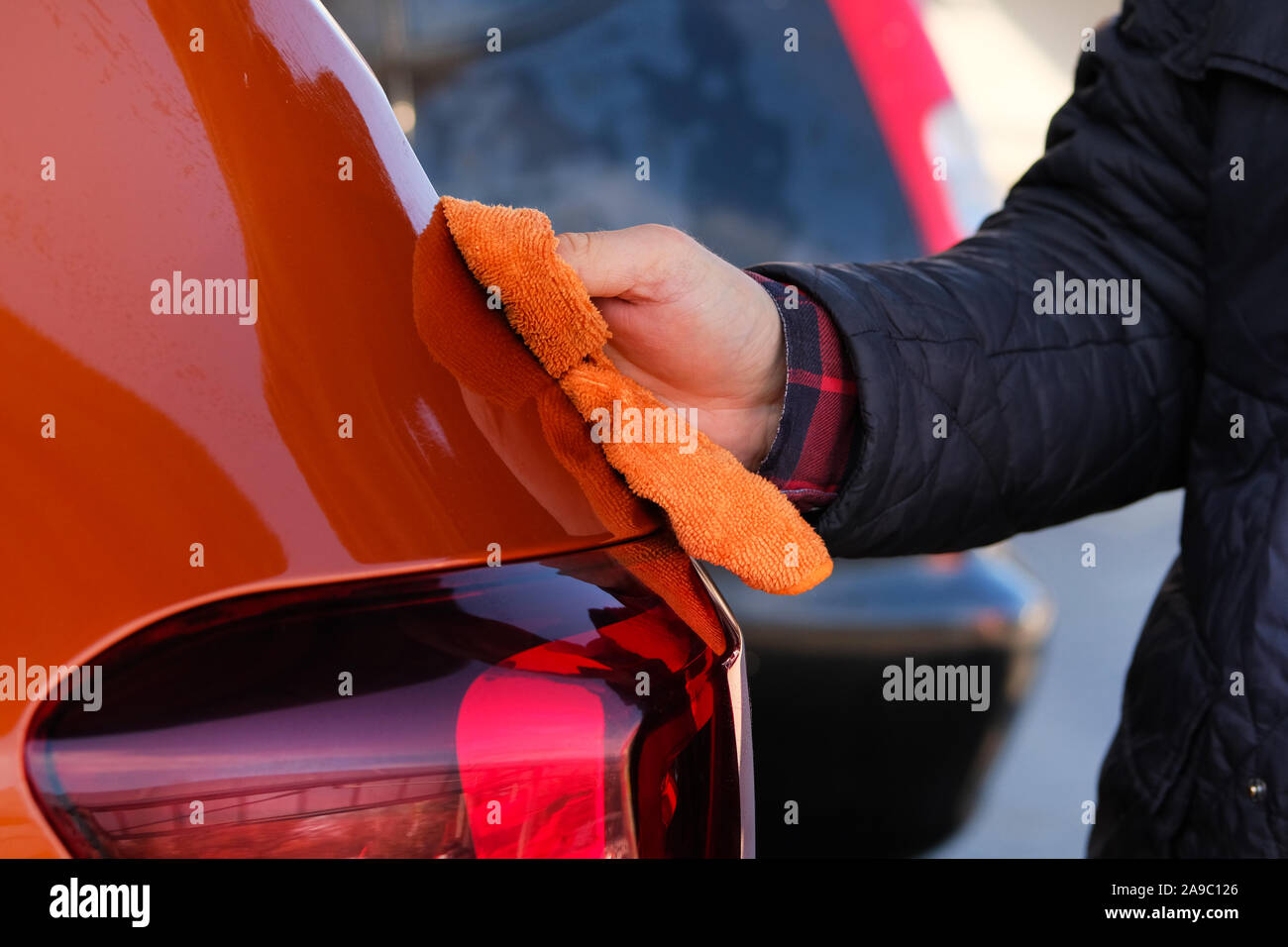 Man after washing wipes his orange car with a rag  at car wash. Male hand and car body close up. Stock Photo